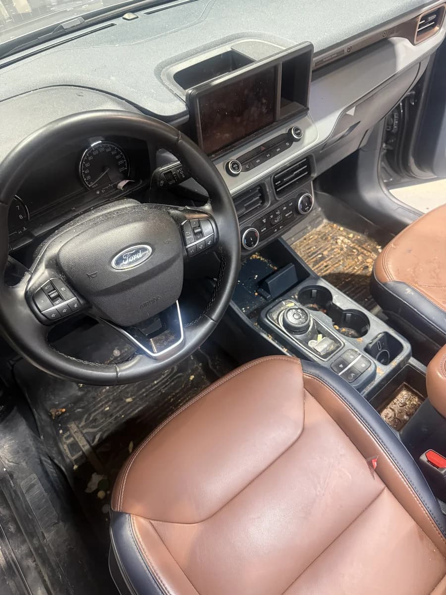 Ford Maverick interior before detailing, with crumbs and debris on the floor mats, console and seats