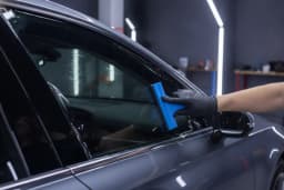 Window tint film being smoothed onto a sedan side window with a squeegee